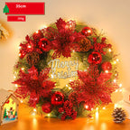 Decorative Christmas wreath with red flowers, lights, and 'Merry Christmas' sign on a wooden surface.