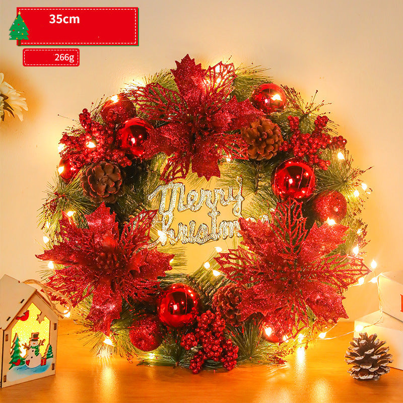 Decorative Christmas wreath with red flowers, lights, and 'Merry Christmas' sign on a wooden surface.